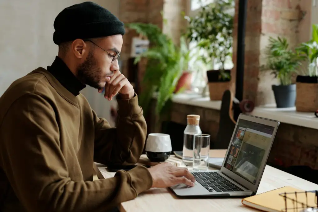 A man in a beanie is seated at a desk, engaged with his laptop, illustrating a moment of concentration.