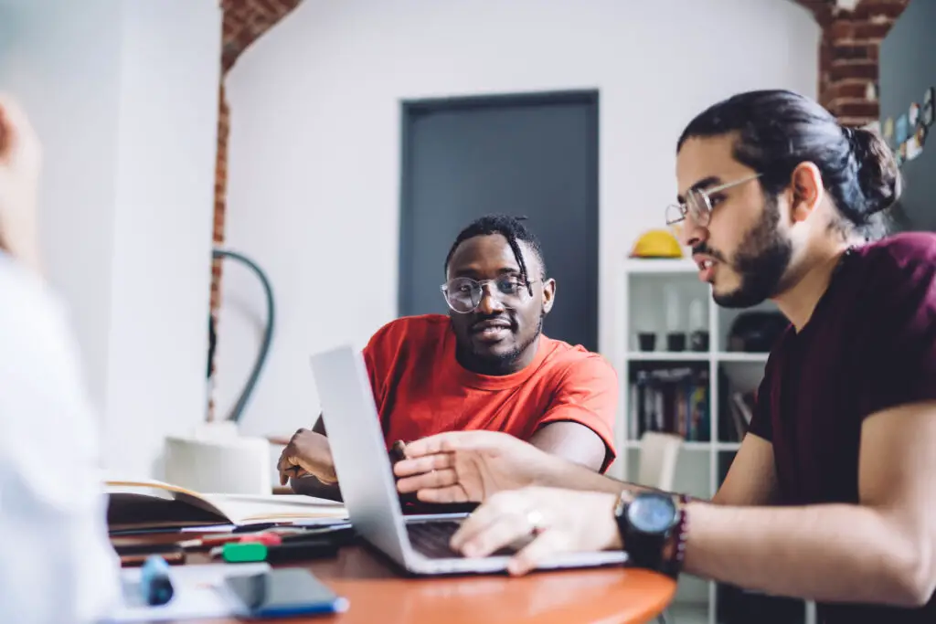 Two men engaged in work, sitting at a table with laptops open, focused on their tasks in a collaborative environment