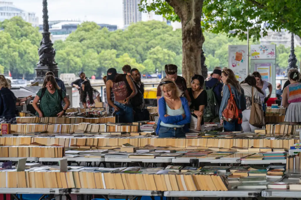 Visitors examine books on a table in a park setting, to minimize college expenses