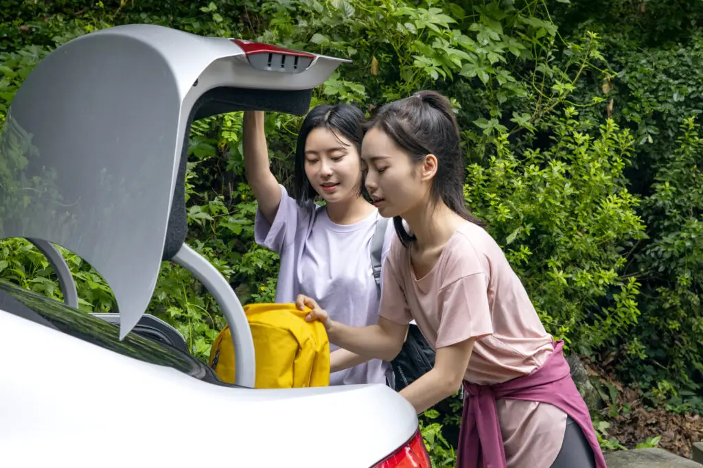 Two women loading a suitcase into a car trunk