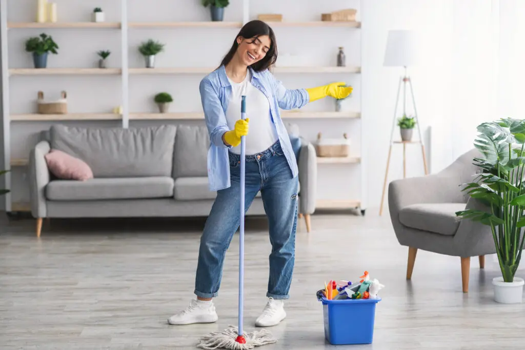 Female college student cleaning living room floor with mop and bucket to achieve good relationships with roommates