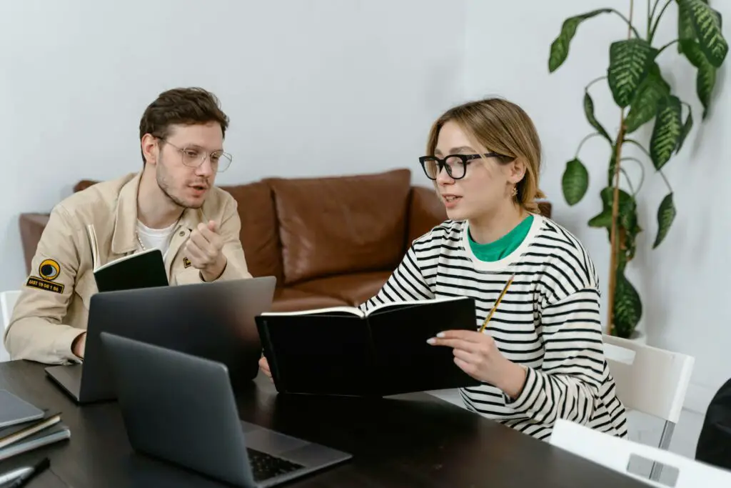 Two individuals working on laptops at a table to achieve good relationships with roommates