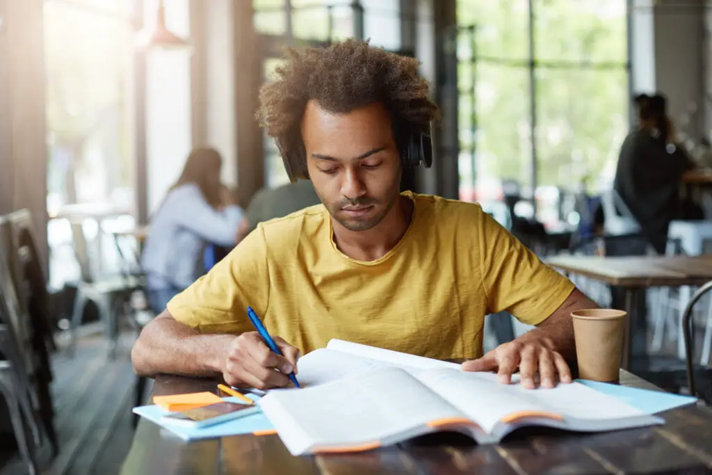 african american male college student wearing headphones finding essay sources in a coffee shop