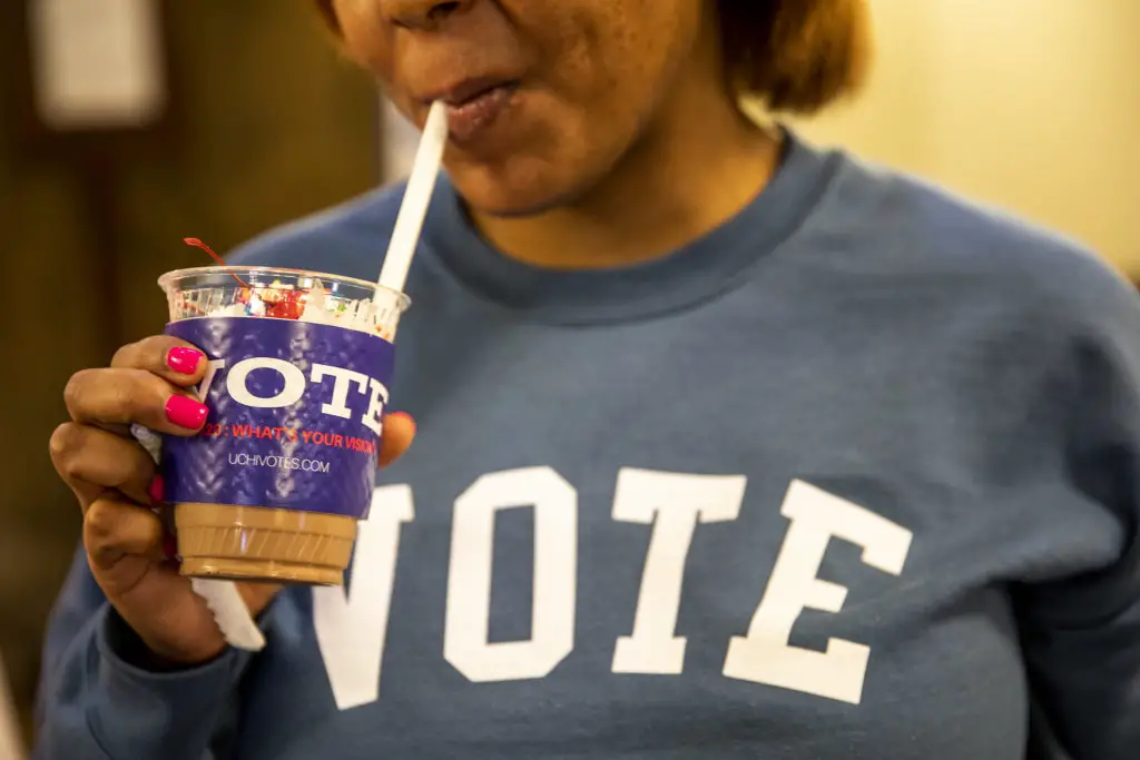 A person wearing a sweater that reads "VOTE" drinks out of a UChiVotes cup