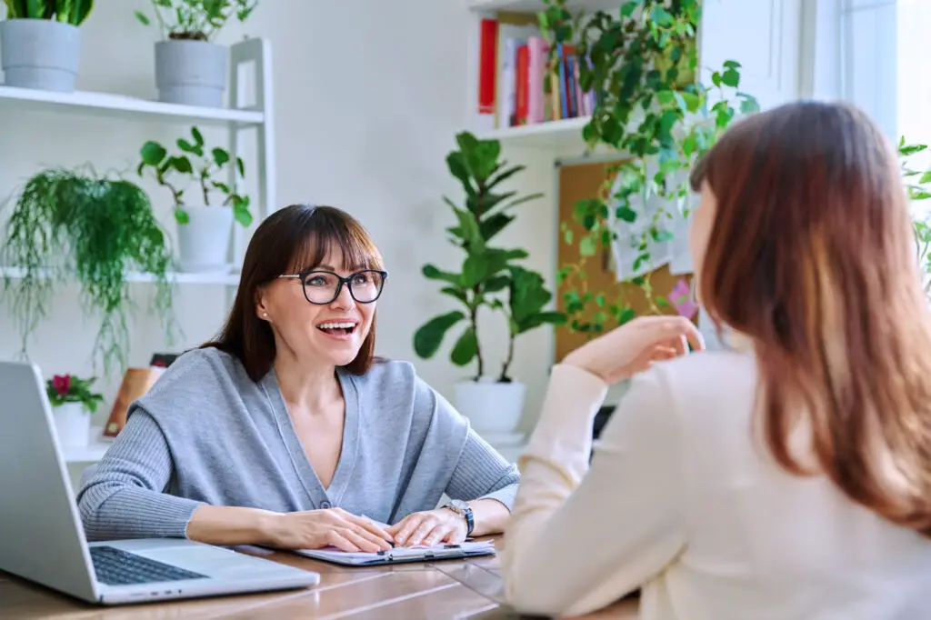 Student and instructor engaged in conversation at a desk in a professional office setting, discussing to maximize remote learning