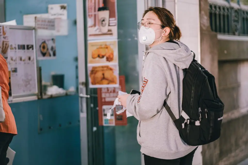 Photo of a woman in face mask waiting in a line to get takeaway food during the coronavirus pandemic