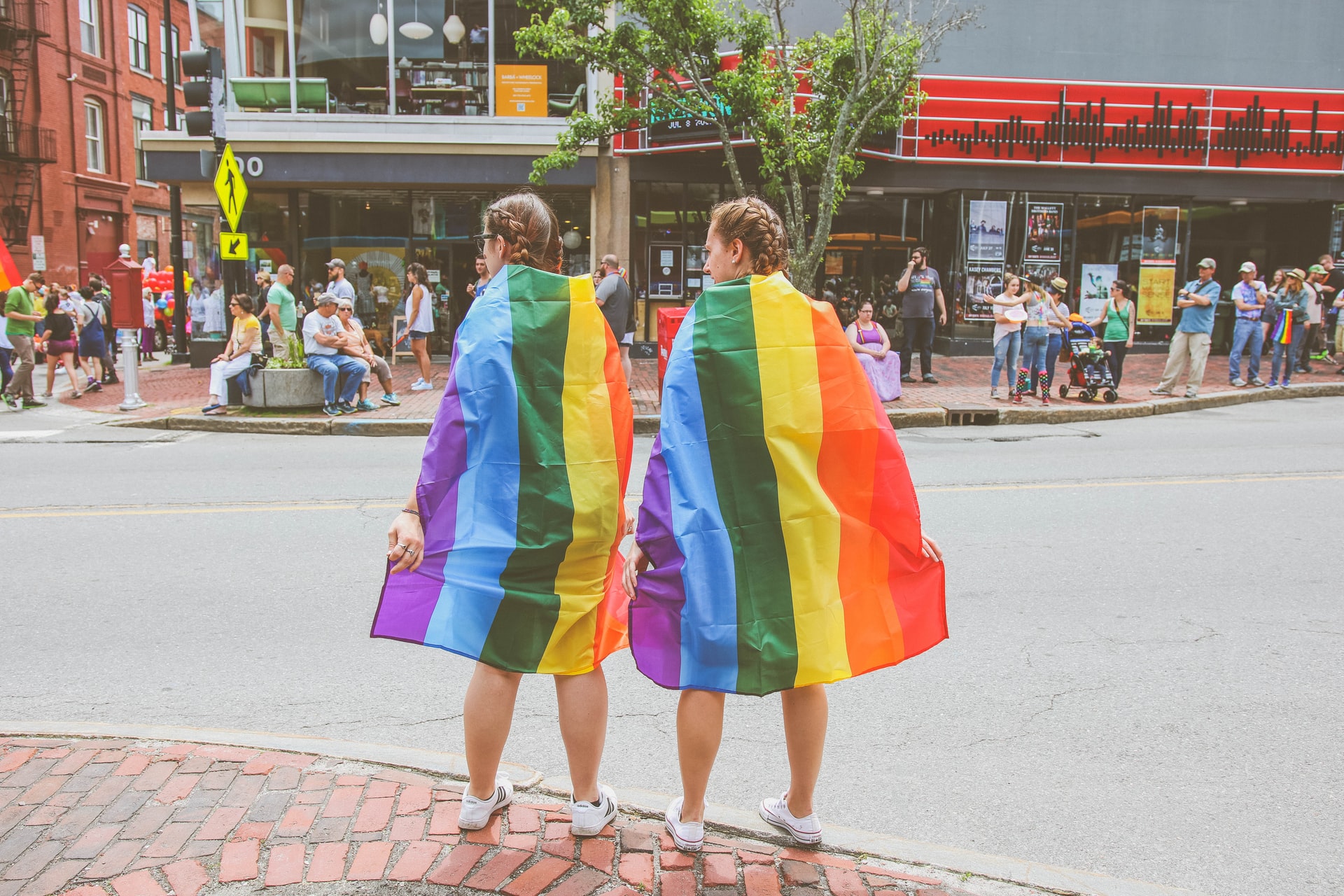 Two women wearing rainbow flags on the street. Photo: Mercedes Mehling/Unsplash