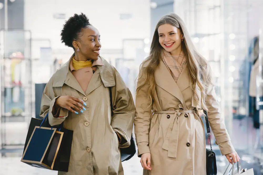 Two happy friends of mixed races wearing coats while carrying shopping bags in a mall 