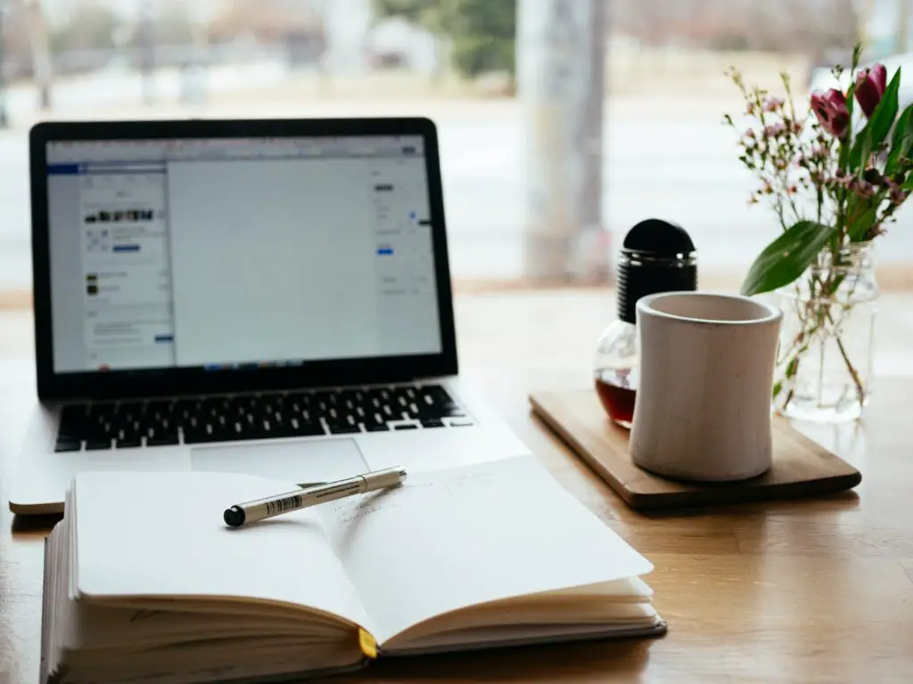 A Macbook Pro near a white notebook.