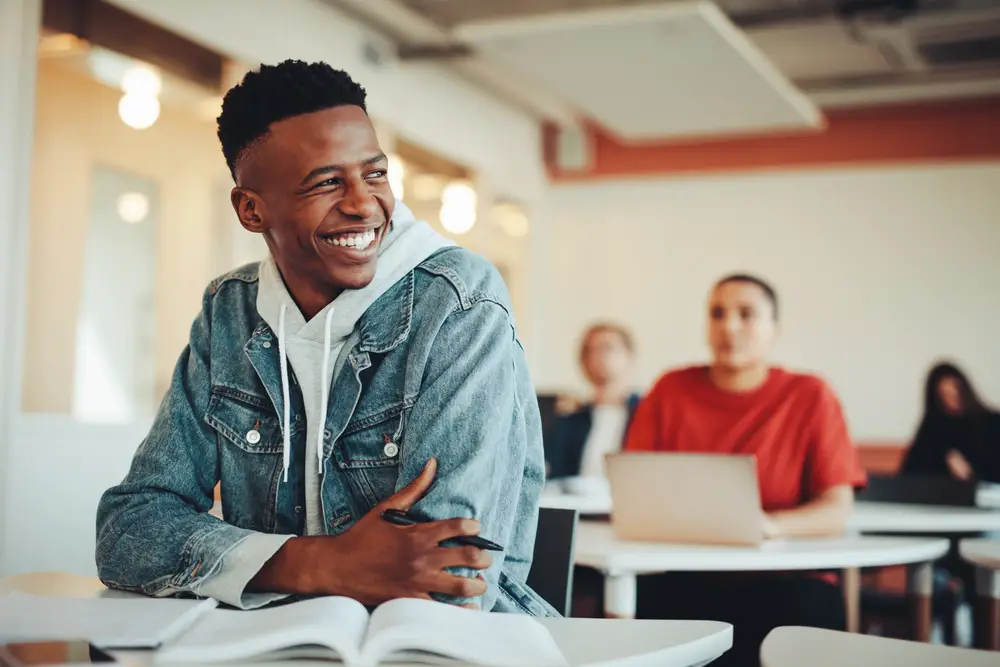 Black male college student sitting in university classroom looking away and smiling