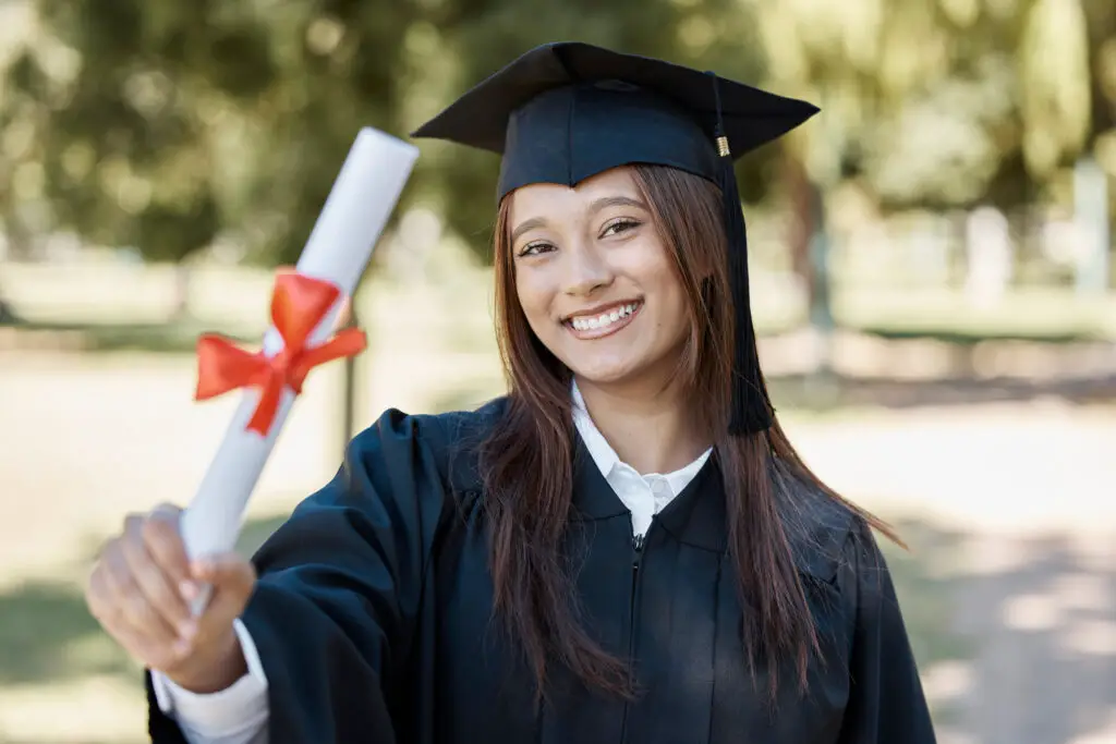 A woman proudly wearing a graduation gown, holding her diploma with a joyful expression on her face