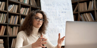 College tutor looking at webcam and talking in classroom giving virtual remote online lesson by zoom