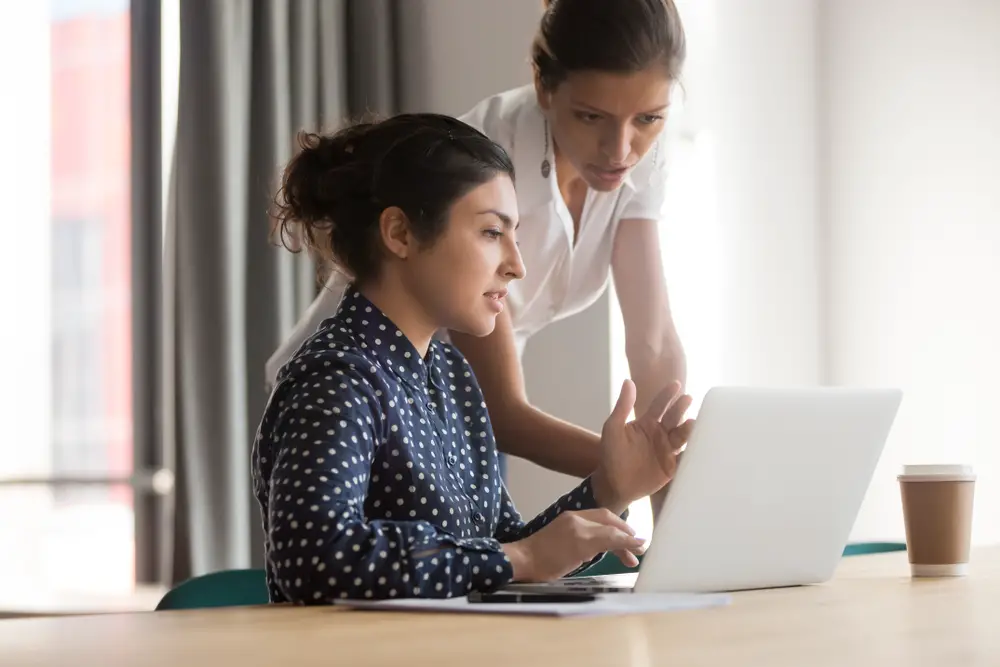 Female mentor and intern talking pointing on laptop at the work desk
