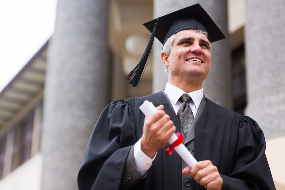 Senior university graduate with diploma in front of college building