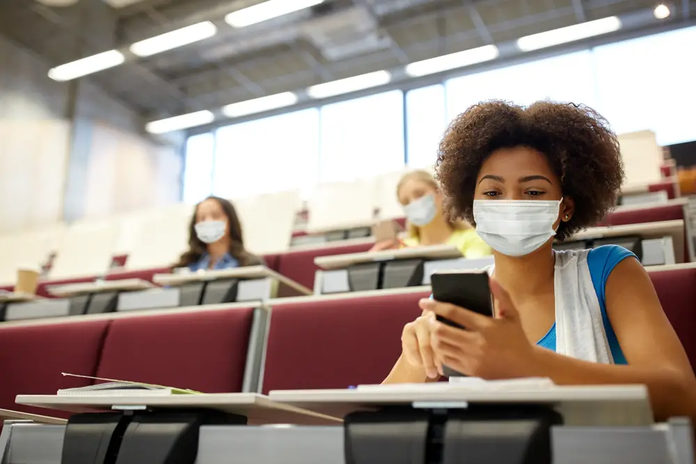 African American college students with mask looking on her phone while sitting in a lecture hall