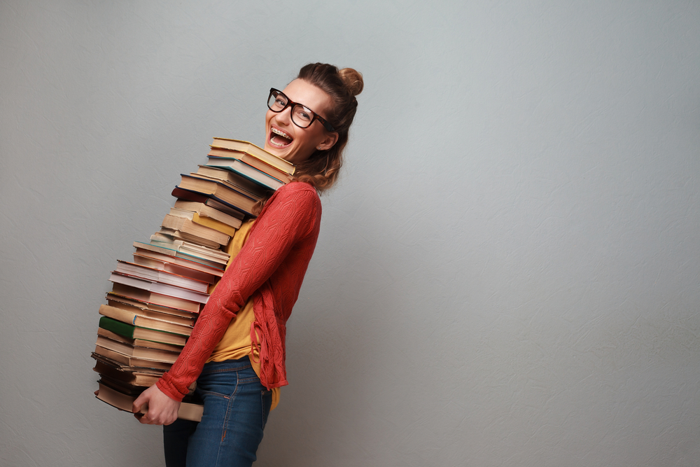 Photo of a student carrying a huge stack of college textbooks