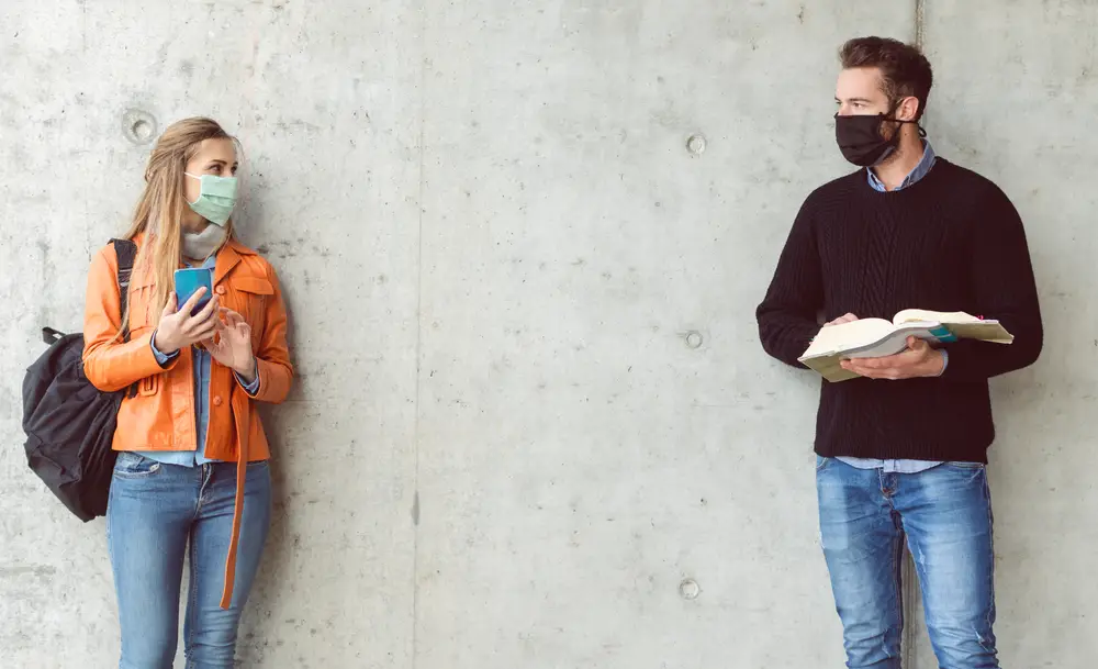 Two students standing in social distance wearing face mask looking at each other