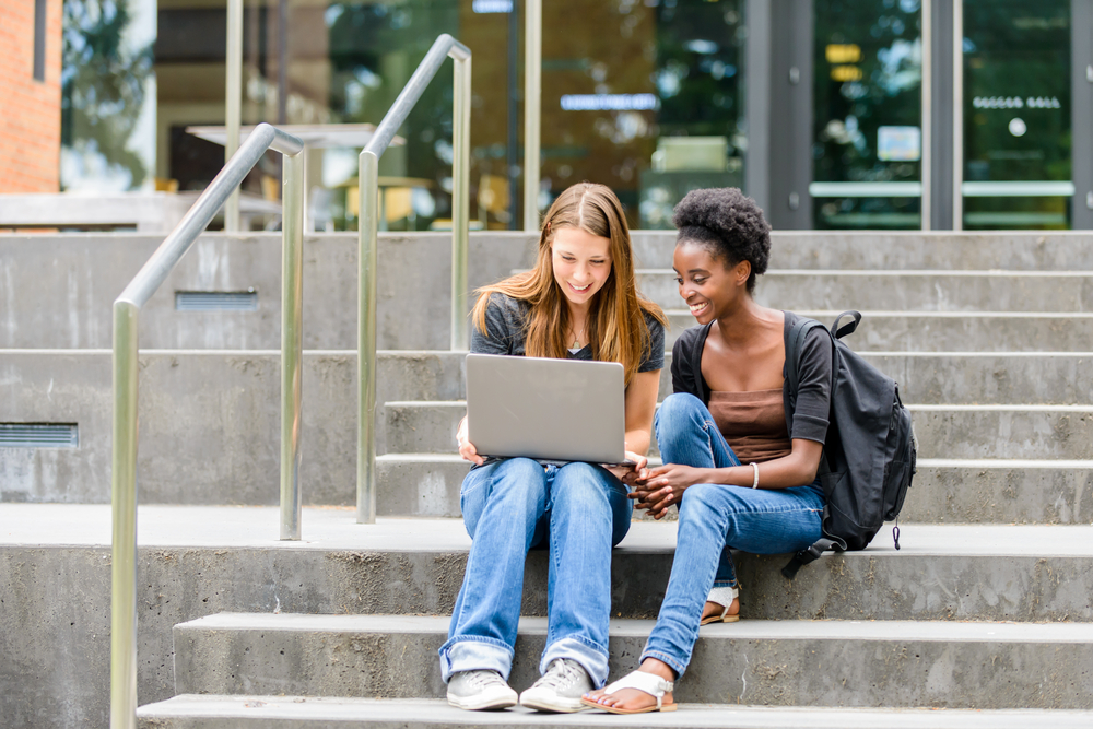 Female college students looking at a laptop, doing some work together on campus