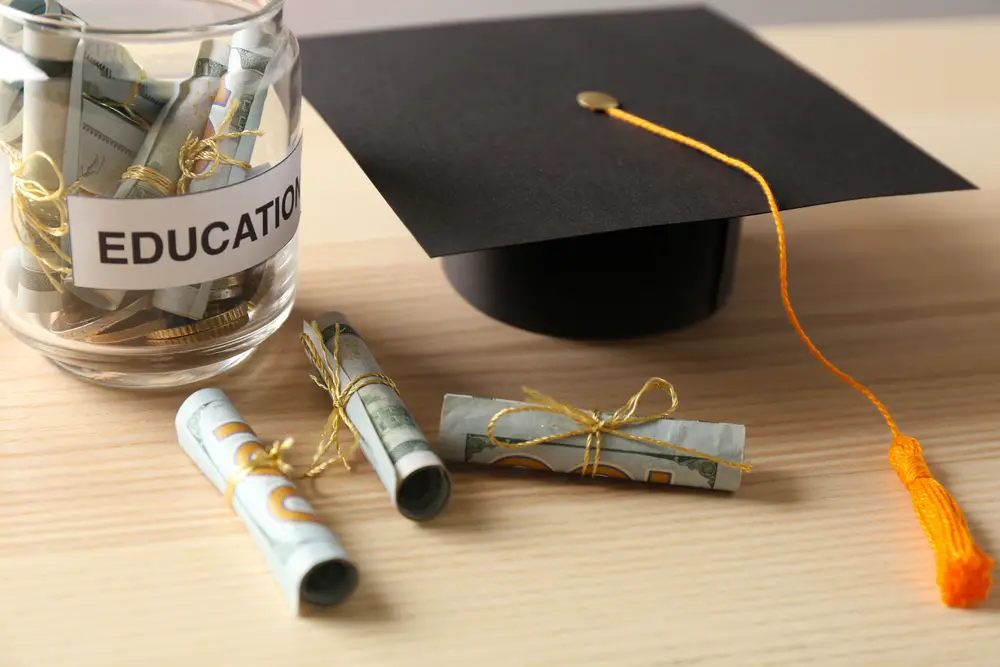 Graduation hat and glass jar with money for education on wooden table