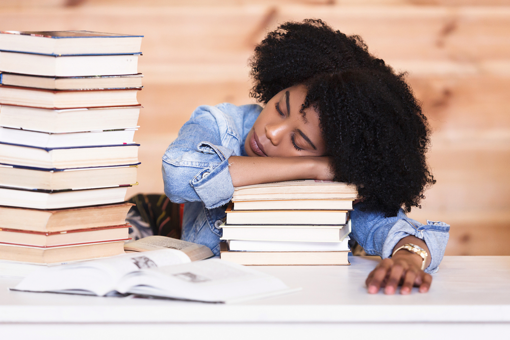 A tired student sleeping on a stack of books