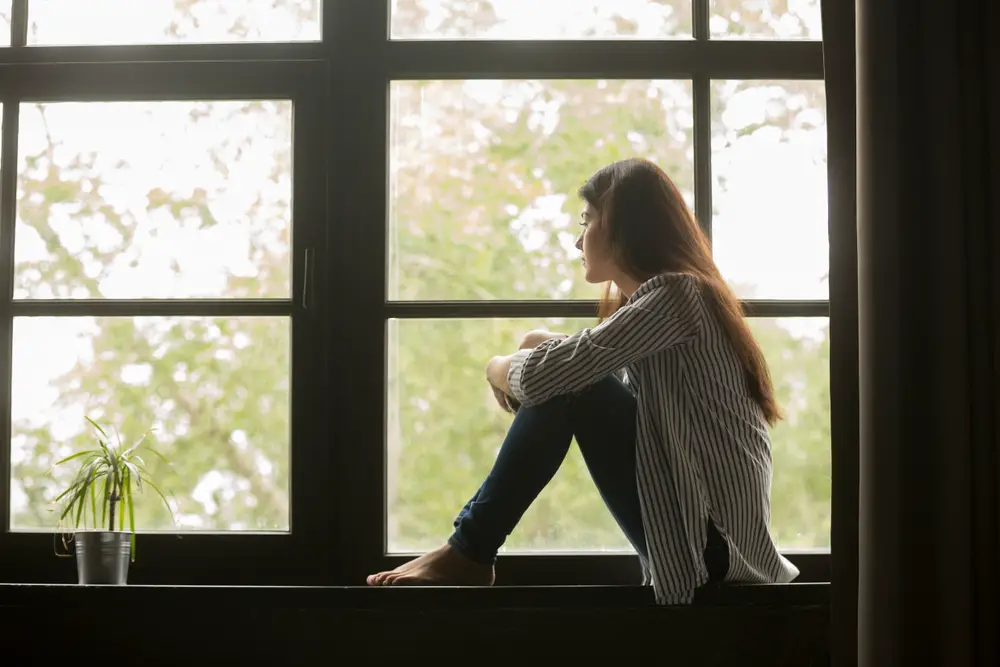 A girl sitting on a window sill looking out of the window
