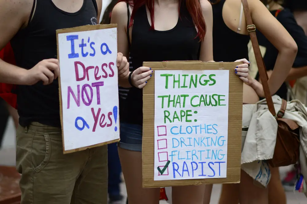 Protestors holding up signs saying 'It's a dress, not a yes!' and one that says only rapists cause rape, not clothing, drinking, or flirting