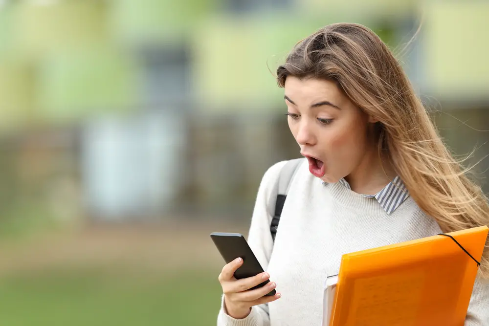 A student is surprised while reading news on her smartphone