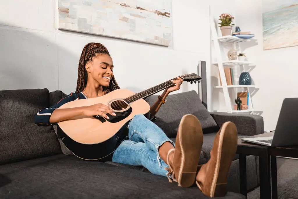 female high school student sitting in a couch playing the guitar