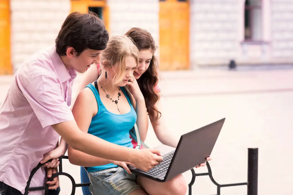 Three young individuals seated on a bench, intently focused on a laptop screen in front of them