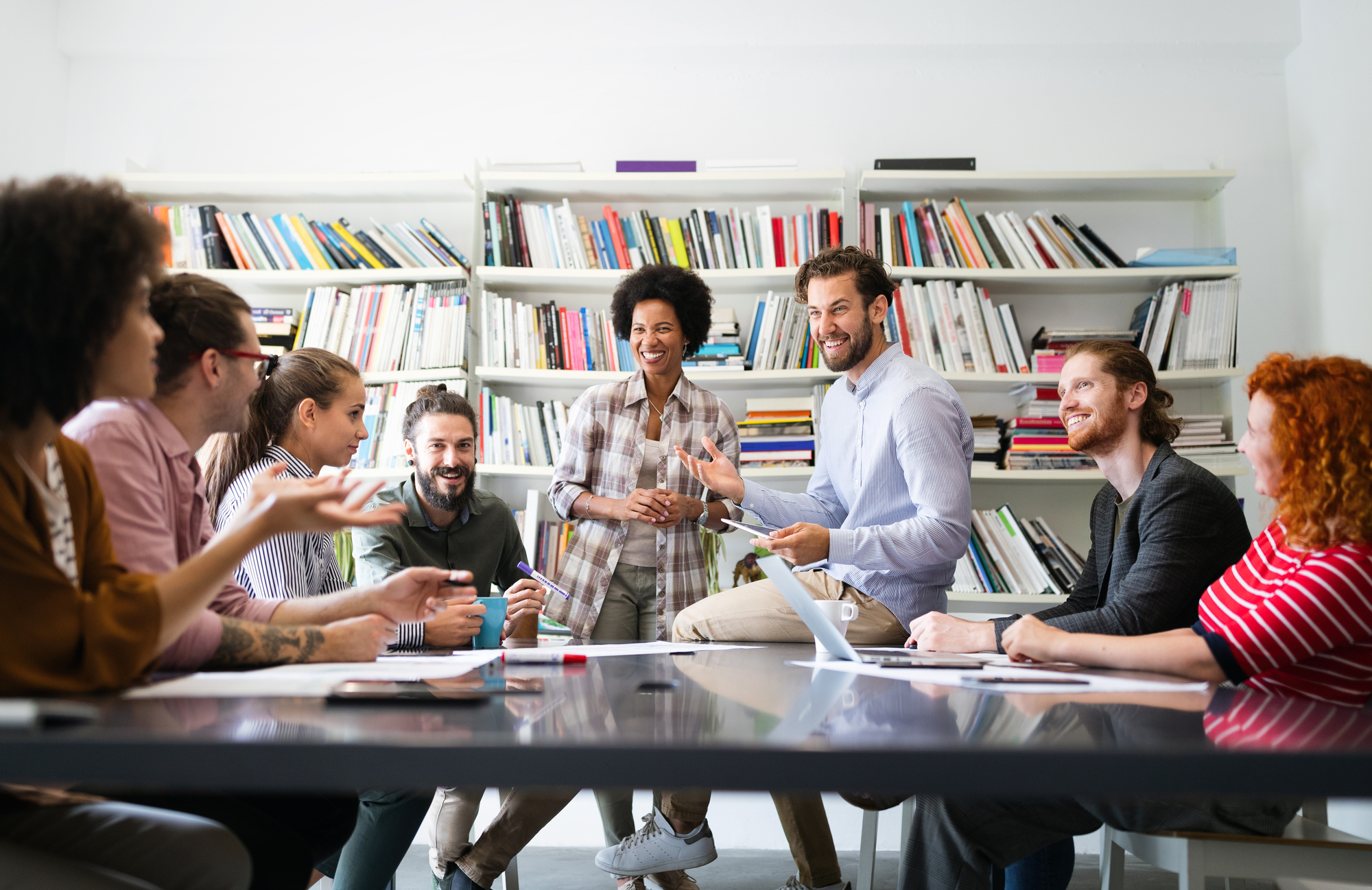 A group of male and female college students discussing college classes cost inside a library