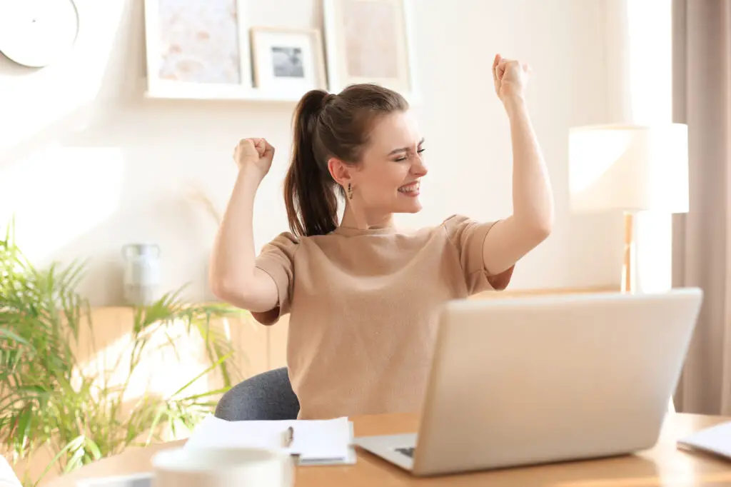 A college student sits at her desk with her arms raised, expressing a moment of triumph on her college application deadlines