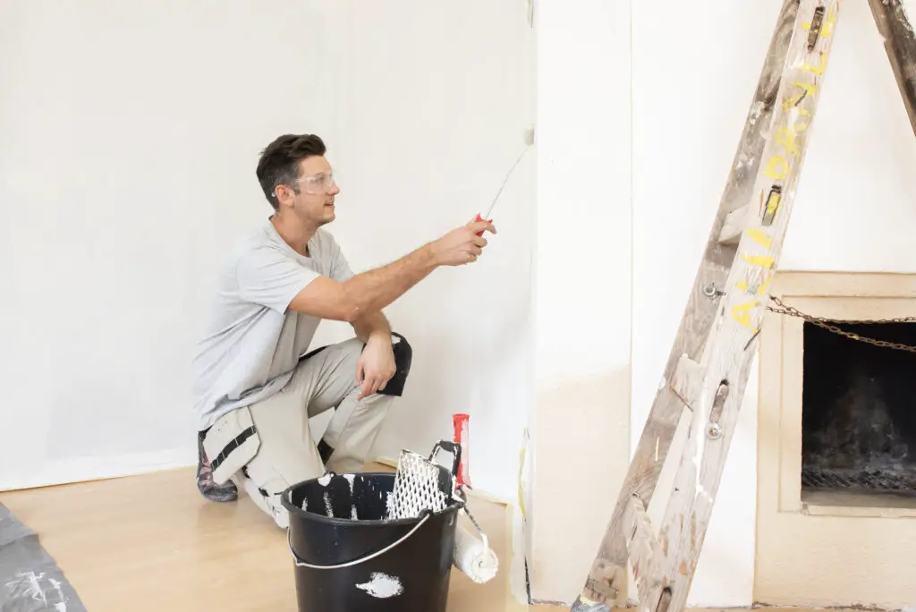 male college student wearing protective eye goggles while painting a wall as a side hustle