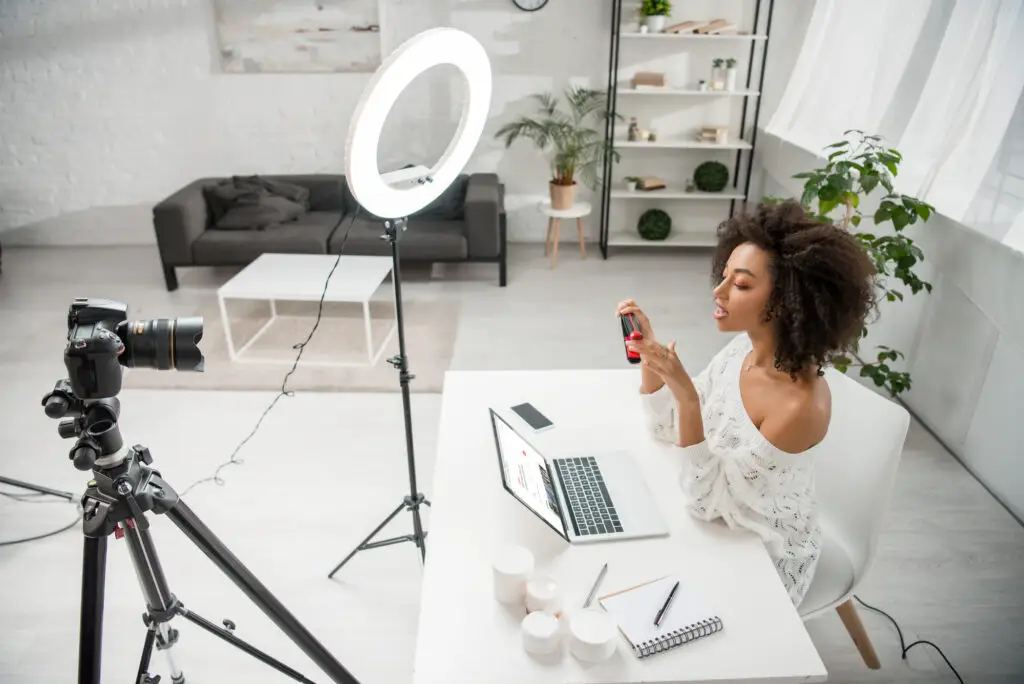 smiling female college student doing a side hustle as an online vlogger inside a studio with camera setup and ring light
