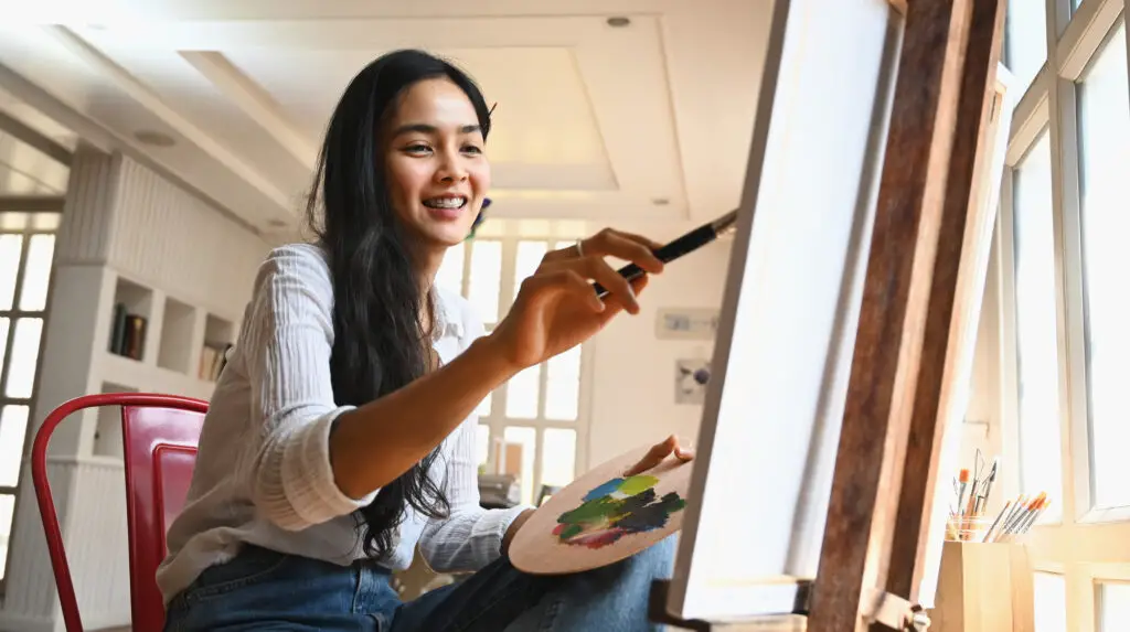 female college student artist holding a paintbrush painting on canvas