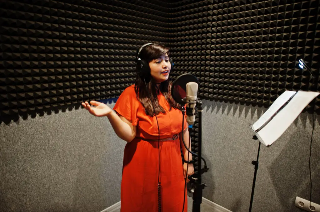 female college student inside a studio booth using headphones and a professional microphone doing voice recording and acting