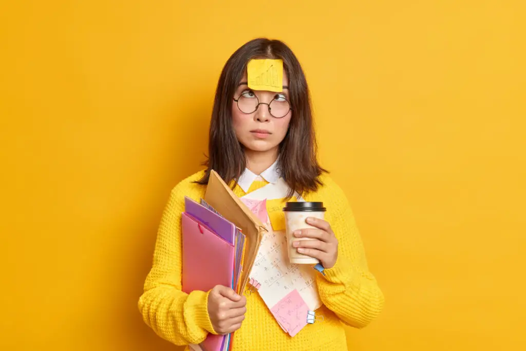 A female student holding papers and a coffee with a sticky note on her face