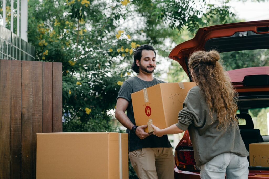 male college student helping a female college student carrying boxes and moving houses as a side hustle