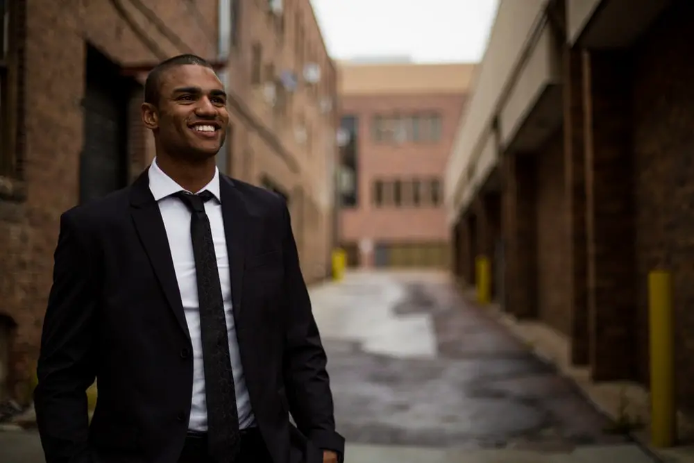 a young man in a suit and tie smiling as he walks in an alley 