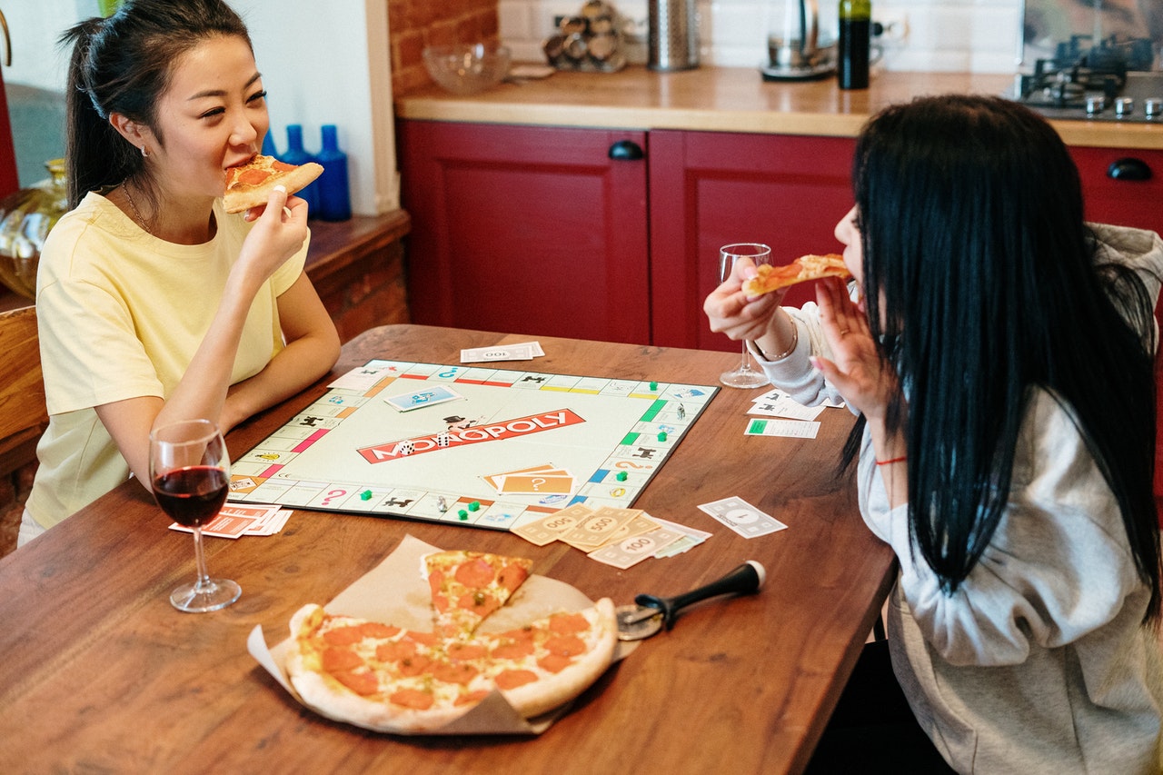 two-female-college-friends-playing-board-game-and-eating-pizza