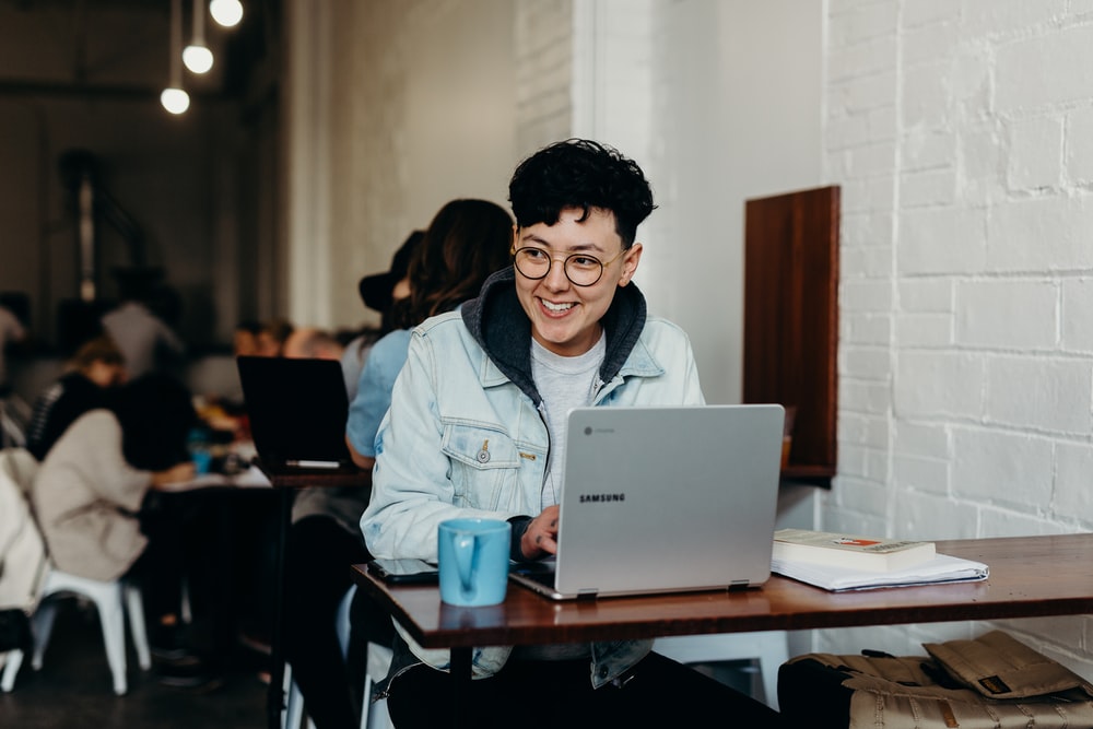 smiling person sitting at a coffee shop and working in front of a laptop 