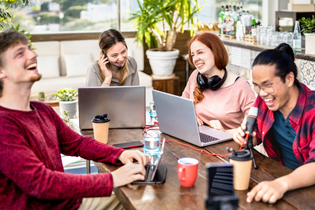 group-of-young-college-interns-laughing-around-table-with-laptops