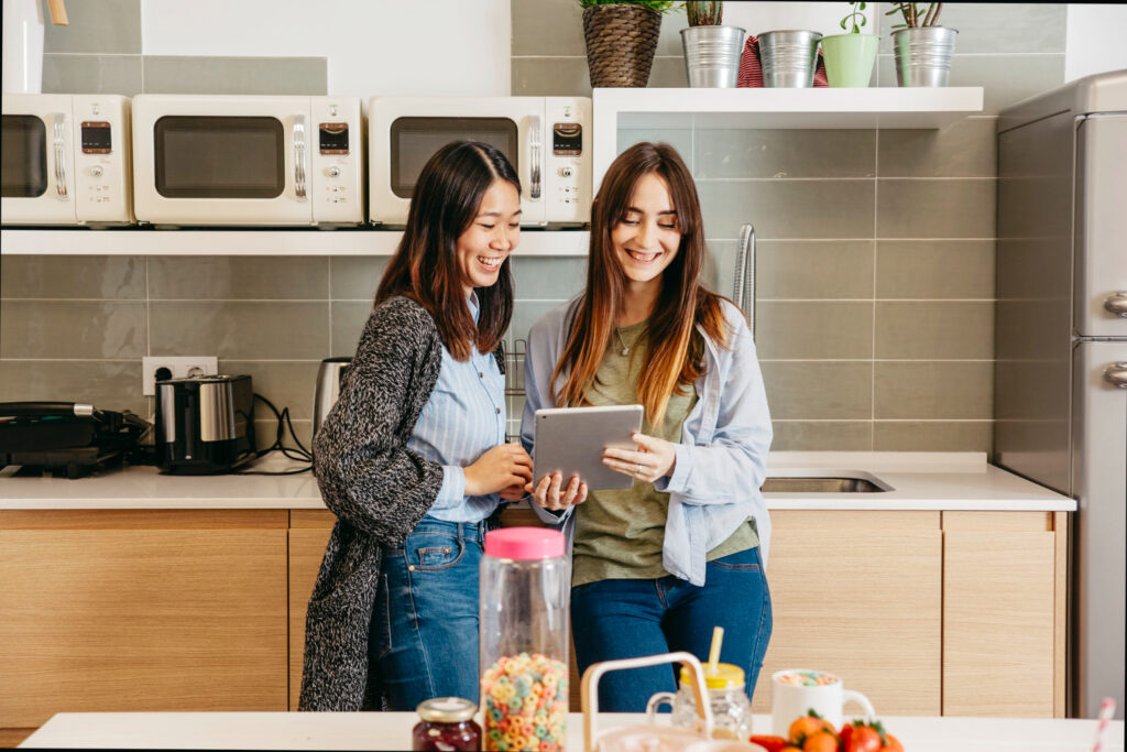 photo-of-two-students-in-college-dorm-kitchen-looking-at-recipe-website-on-tablet