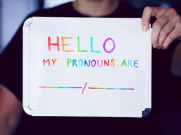 a person holding up a whiteboard advocating for lgbt pronouns