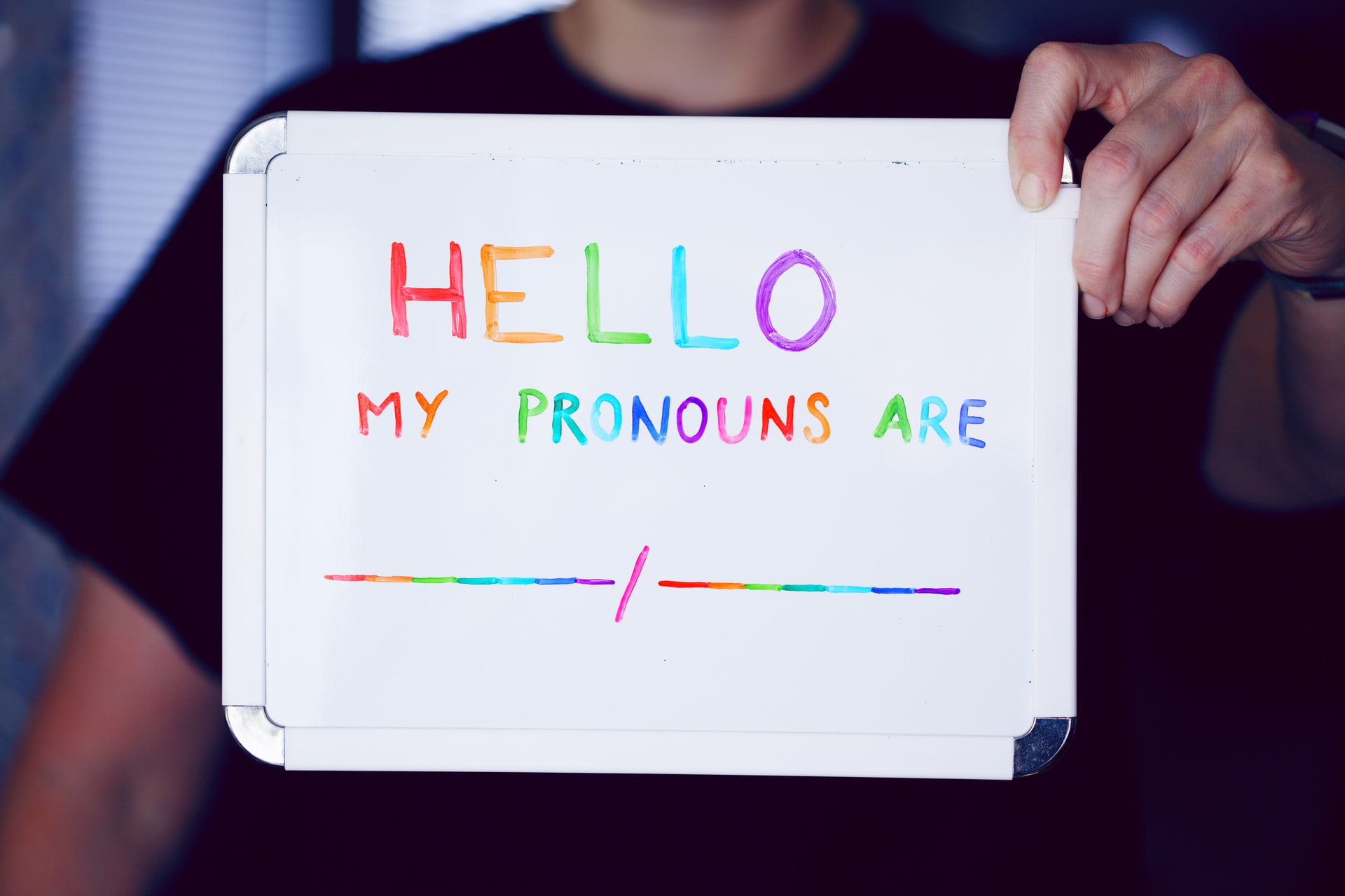 a person holding up a whiteboard advocating for lgbt pronouns