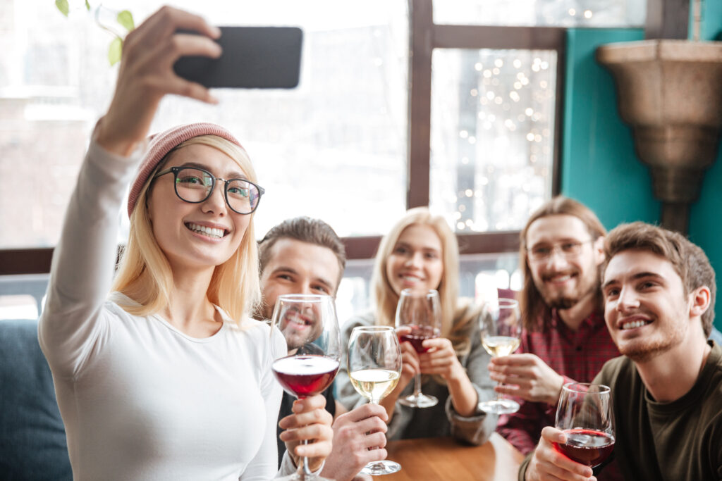 Photo of cheerful friends sitting in cafe and drinking alcohol and make a selfie by phone