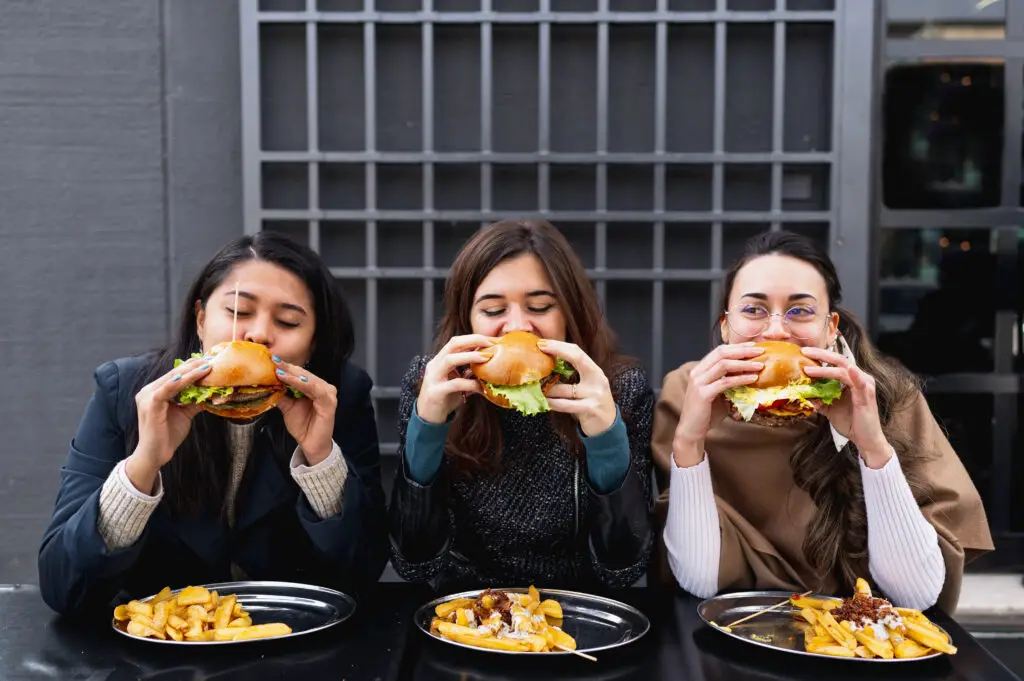 Women sitting at table restaurant biting burgers