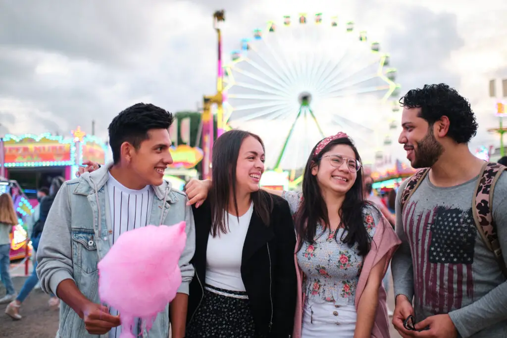 Group of young friends with cotton candy talking and enjoying the time together in an amusement park