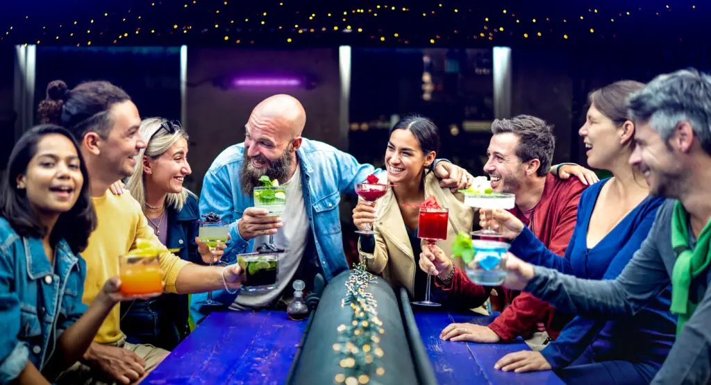 Multicultural people toasting multicolored fancy drinks at a bar