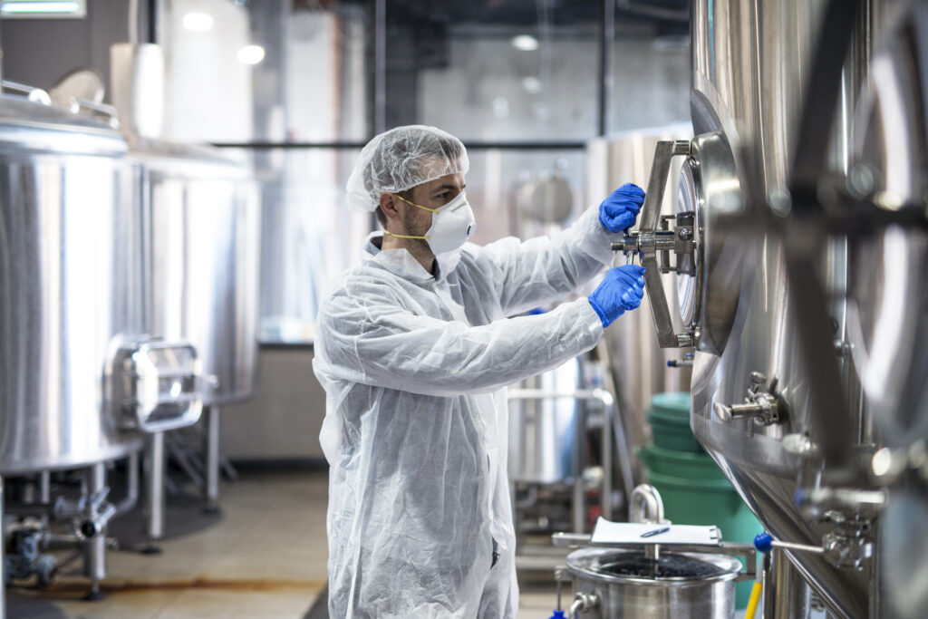 Technologist in protective uniform wearing hairnet mask goggles and gloves