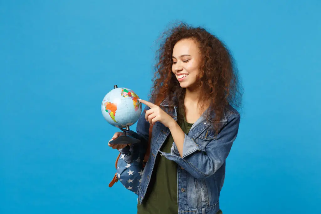 Young African American girl teen student in denim clothes, backpack holds globe